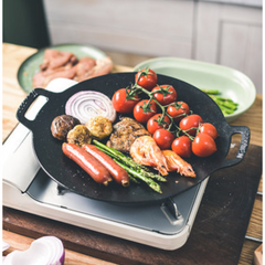 Black cast iron skillet with assorted food on a portable stove